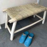 Banc marocain en bois fait main avec siège en raphia en osier, debout dans le hall d'entrée, avec des pantoufles devant