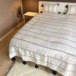 Witte Marokkaanse handgeweven sprei met zwarte strepen en zwarte pompons op bed met bijpassende kussens