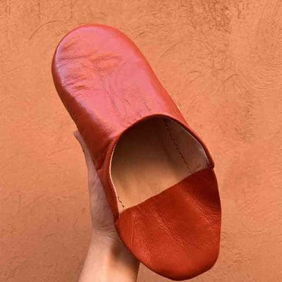 Chaussons marocains faits main en terre cuite, avec mur orange derrière