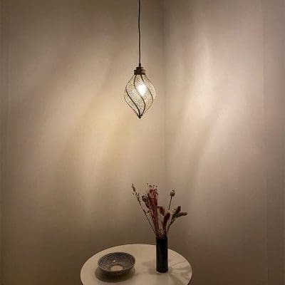 Marokkanische handgefertigte, sich drehende Tropfenlampe, die über einem dekorativen Tisch hängt und im Dunkeln beleuchtet wird