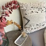 Marokkansk håndvevd putetrekk i beige med ulldetaljer på sidene, med svart stripemønster, liggende i et sofahjørne