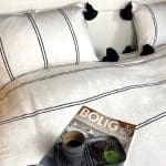 Witte Marokkaanse handgeweven sprei met zwarte strepen en zwarte pompons, met bijpassende kussens en een dienblad met snacks erop