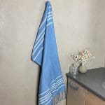 Serviette de hammam marocaine tissée à la main en bleu accrochée à un crochet dans une salle de bains