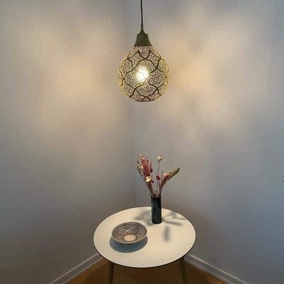 Marokkansk håndlavet rund lampe af guld, hængende over et dekorationsbord i et hjørne