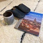 Marokkanske slippers oven på Beni Ouarain tæpper med Marrakech guide og krus ved siden af