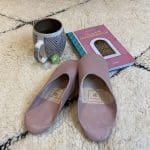 Marokkaanse handgemaakte pantoffels in lichtviolet bovenop een Beni Ouarain-vloerkleed met Marrakech-gids en mok ernaast