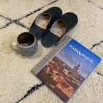 Marokkanske slippers oven på Beni Ouarain tæpper med Marrakech guide og krus ved siden af