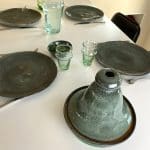 Vier marokkanische Teller und eine Tajine-Schale aus grünem Marmor auf einem gedeckten Tisch mit Beldi-Glas