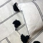 Witte Marokkaanse handgeweven sprei met zwarte strepen en zwarte pompons, met bijpassende kussens, dicht