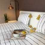 Witte Marokkaanse handgeweven sprei met zwarte strepen en gele pompons, met bijpassende kussens en ontbijtbord erbovenop