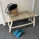 Banc marocain en bois fait main avec siège en osier raphia, debout dans le hall d'entrée, avec un sac sur le dessus et des pantoufles devant