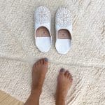 Marokkanske håndlavede slippers i hvid med mønster oven på beni ouarain tæppe med fodmodel ved siden af