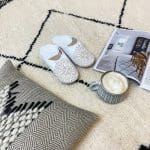 Marokkanske håndlavede slippers i hvid med mønster oven på beni ouarain tæppe, med andre marokkanske produkter ved siden af
