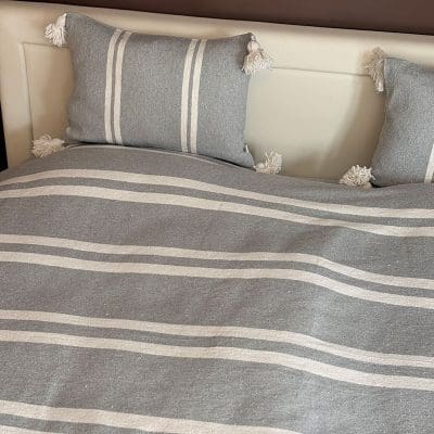 Prachtige katoenen sprei, handgemaakt in Marokko. Grijs-wit gestreept met pompons in elke hoek.